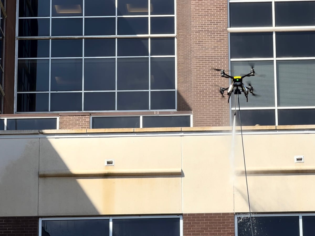 Rotag PT Services cleaning drone works beside exterior louvers on a commercial facade.