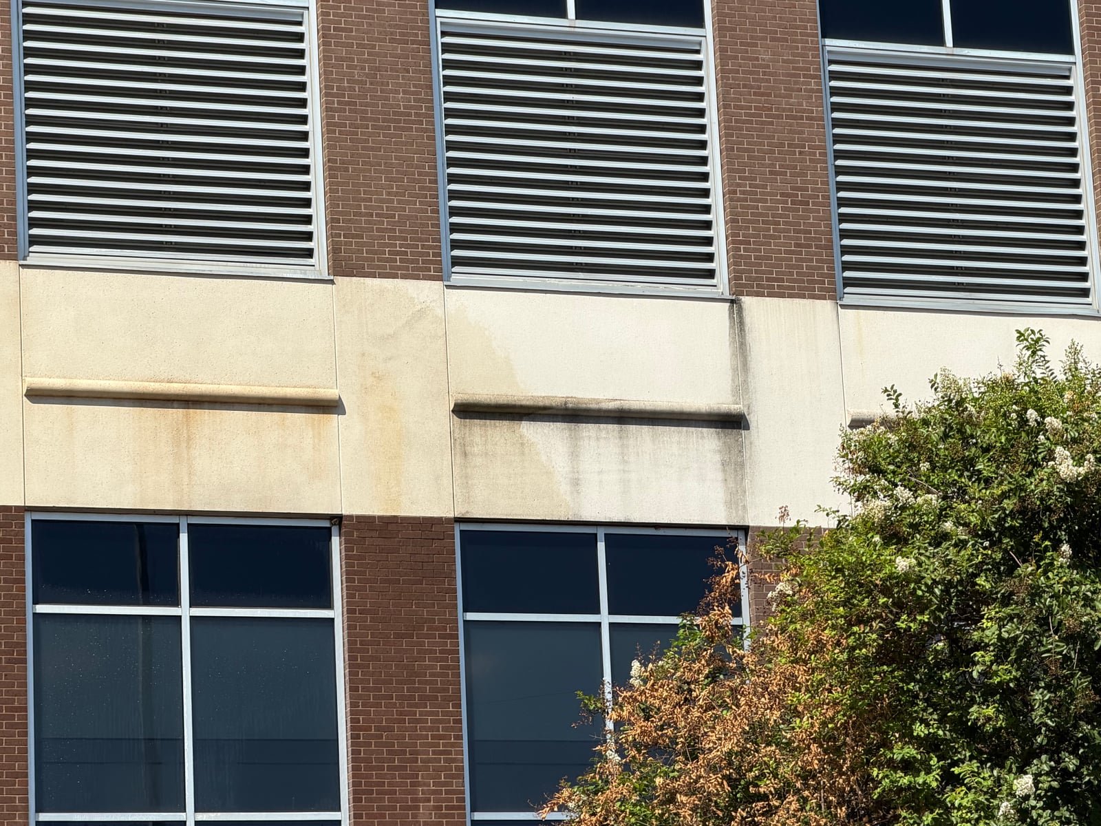 Commercial facade before cleaning, with dark runoff staining visible beneath exterior louvers.